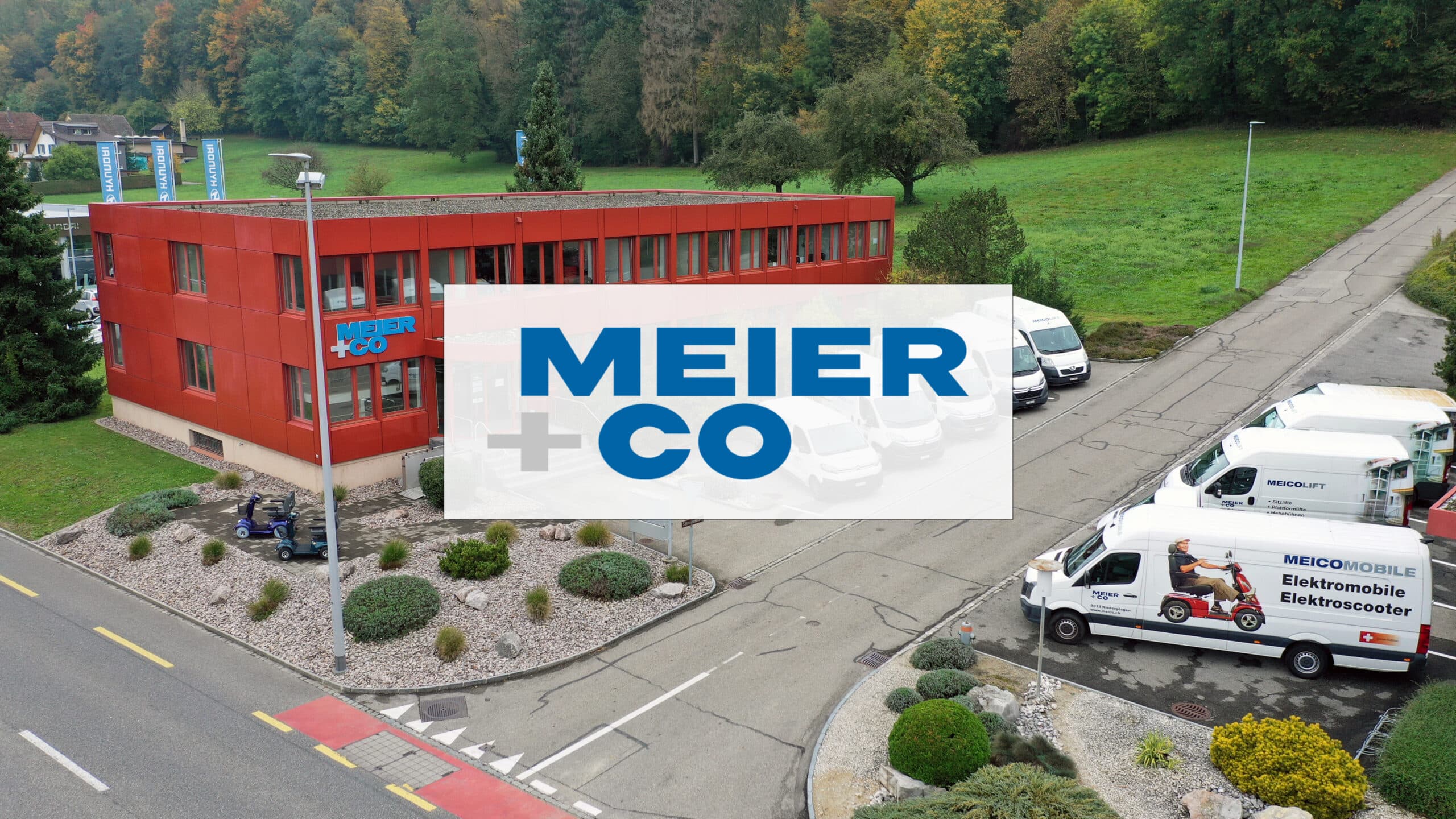 Drönarfoto av Meier + Co AG:s lokaler i Niedergösgen, Schweiz. Röd byggnad med vita fordon parkerade snett framför i grönt landskap.